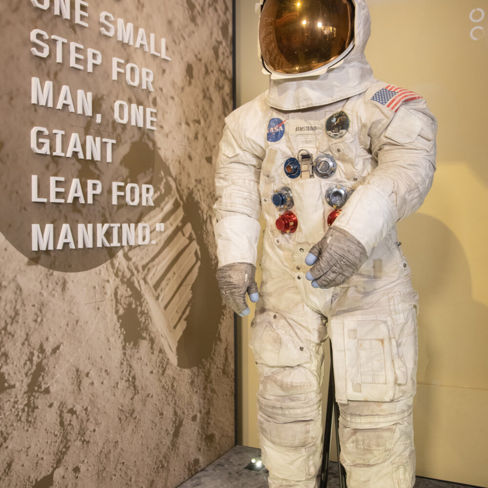 Neil Armstrong’s spacesuit on display with his words from the moon landing "That’s one small step for man, one giant leap for mankind in the background.